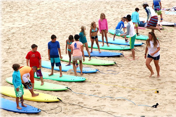 A row of students standing on surfboards on the beach