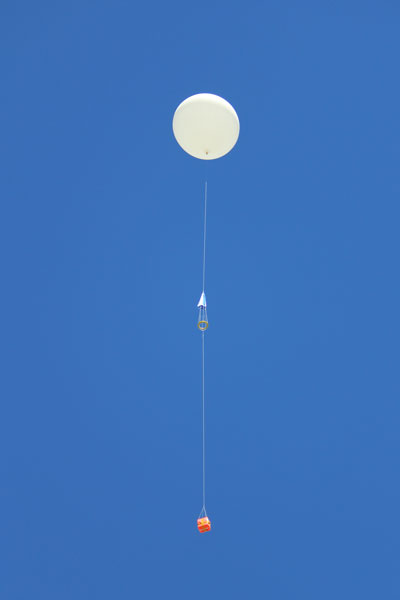 A white balloon with a red payload flying in a blue sky