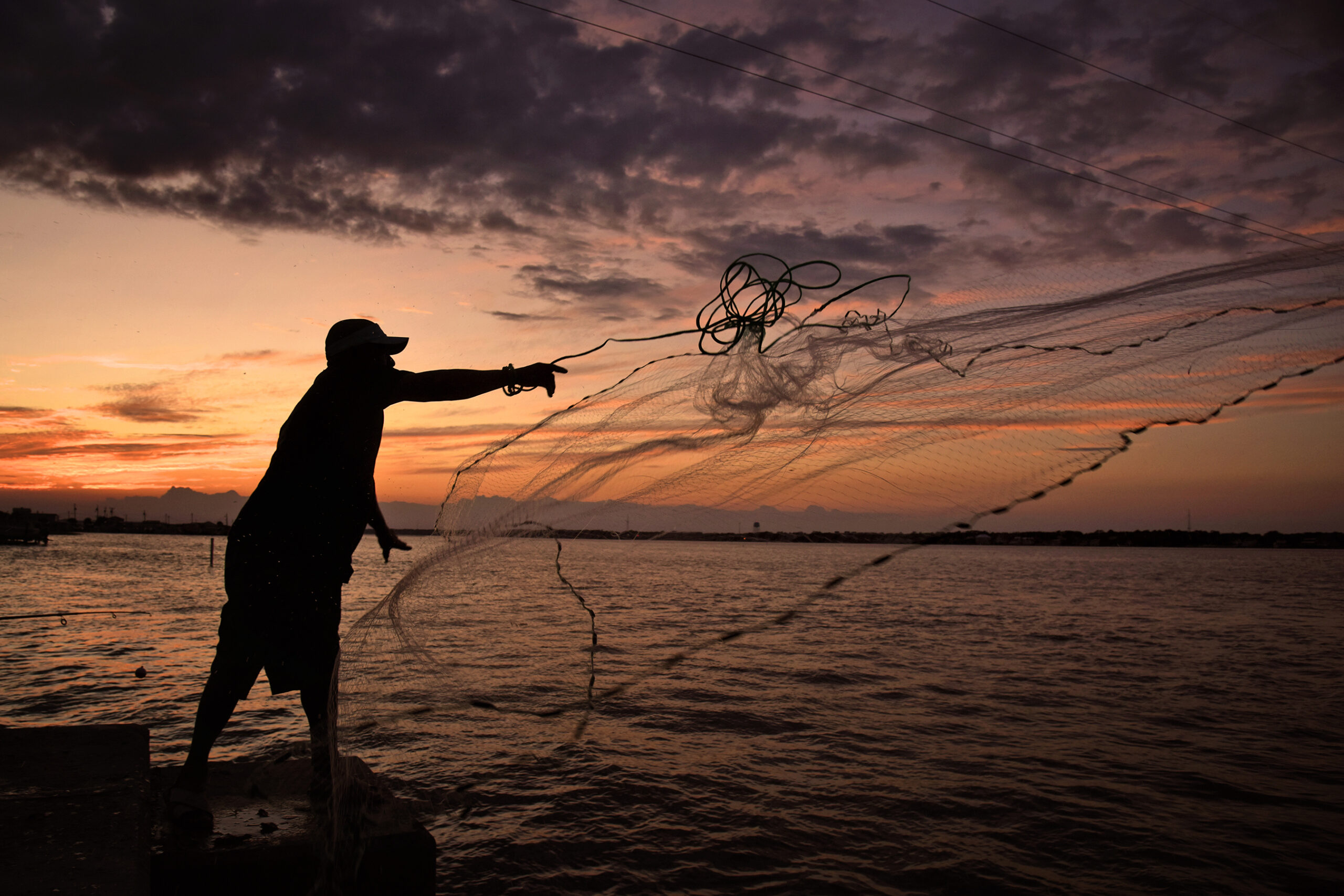 A silhouette casting a net at sunset