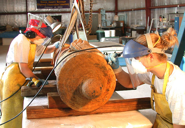 Conservators use air scribes to painstakingly remove concretion from a recovered cannon.