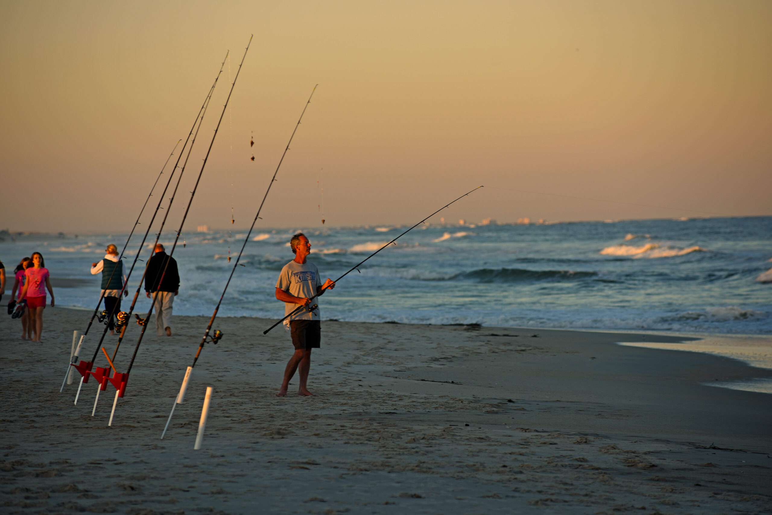 image: a man fishes from the beach.