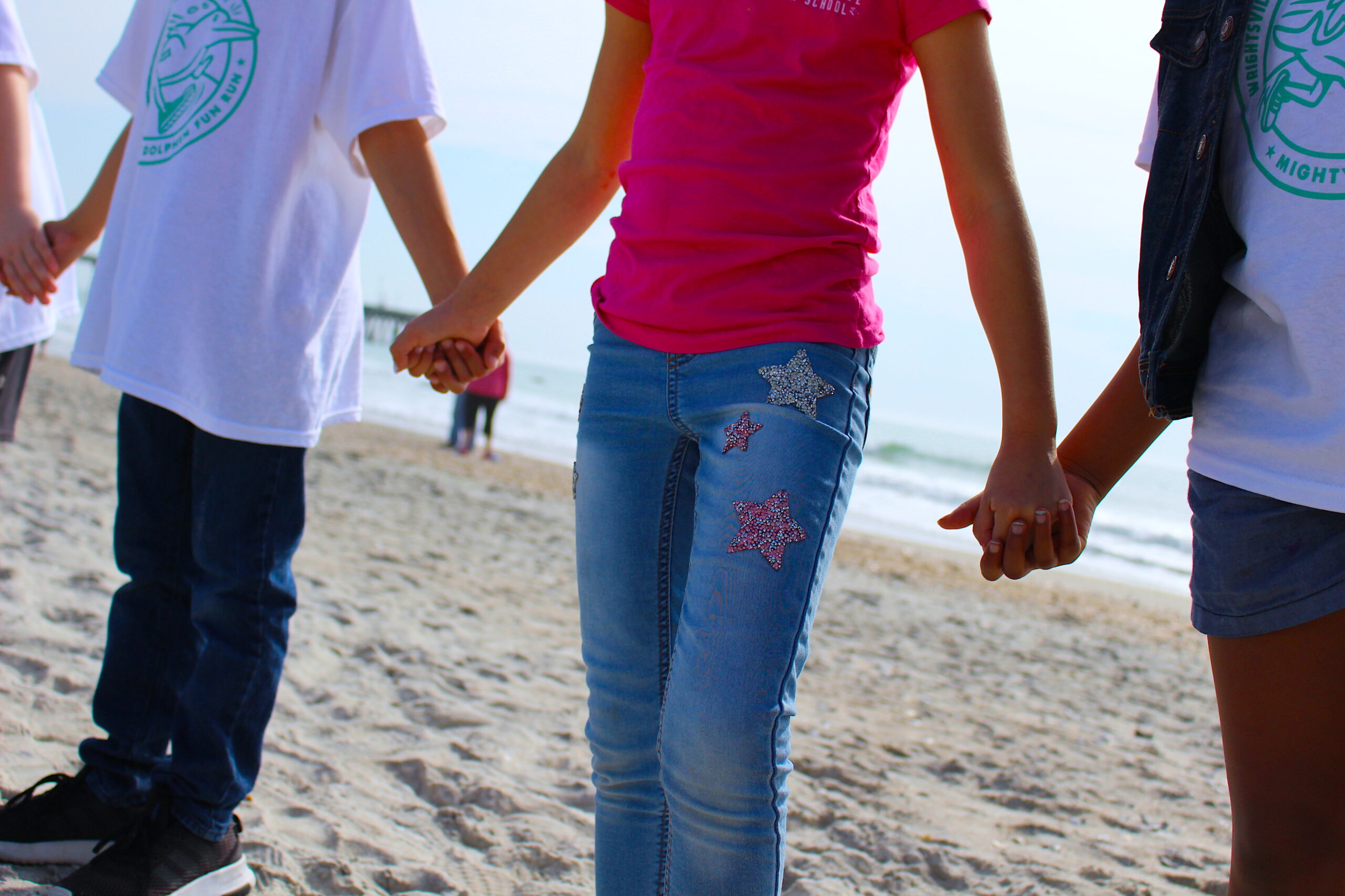 3 children holding hands on a beach.