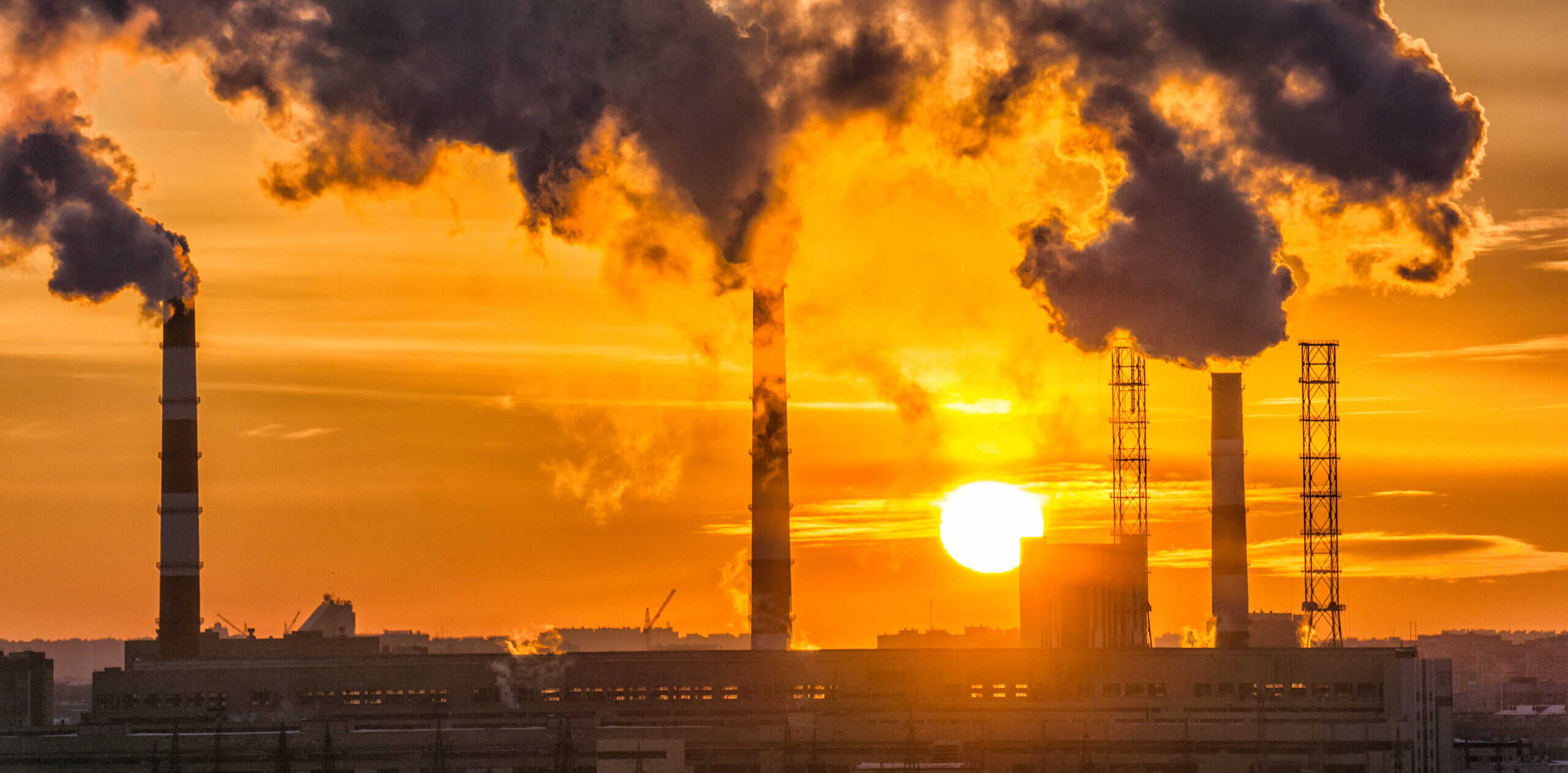 image: factory smokestacks release smoke into the air during sunset.