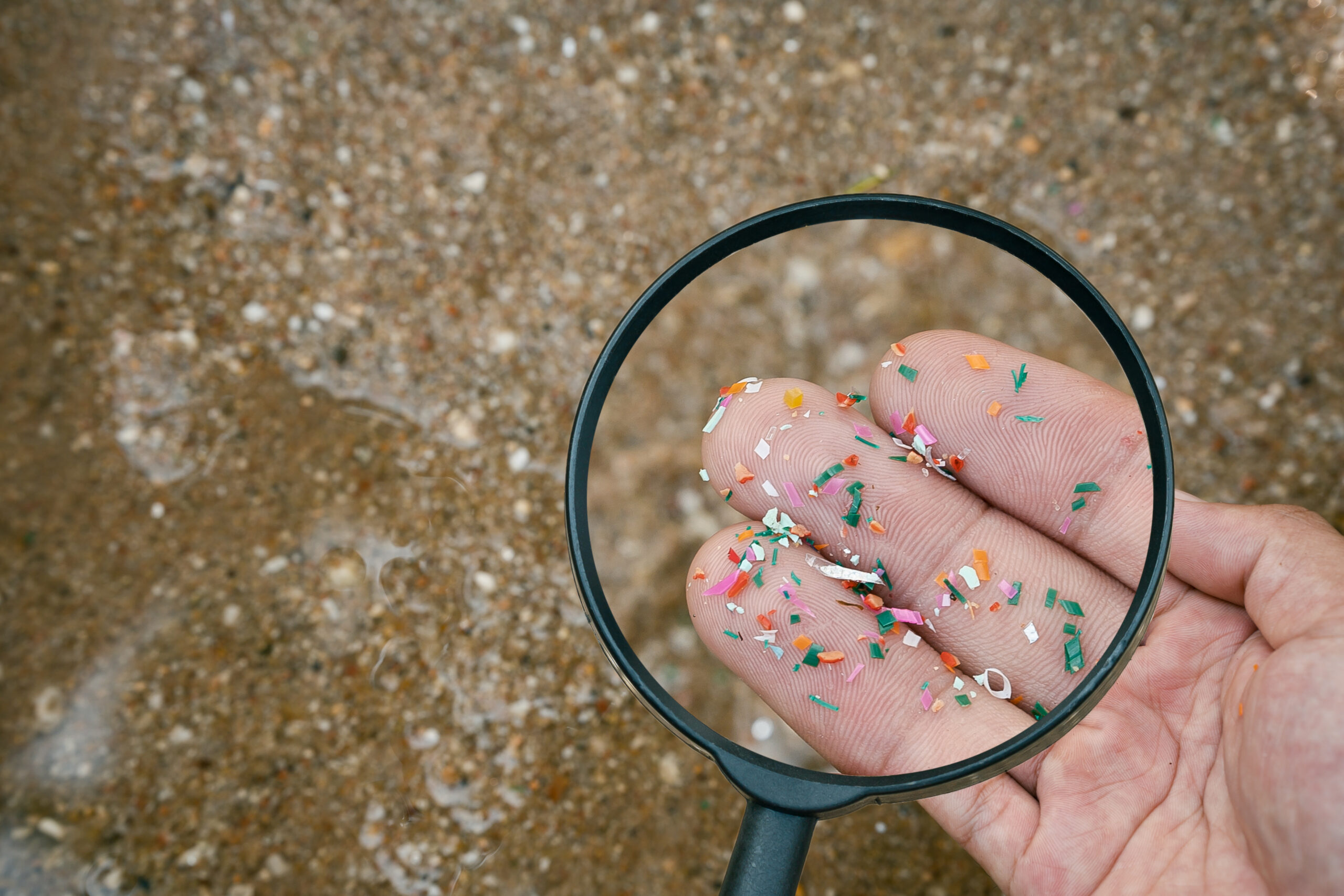 a magnifying glass over a hand showing many microplastic pieces