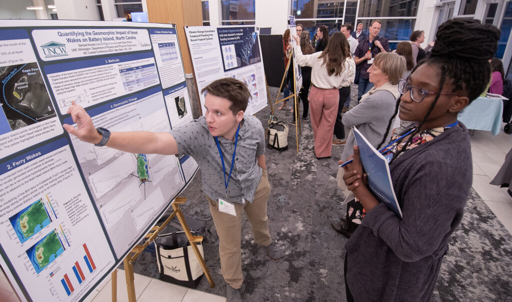 image: UNC Wilmington student Sam Krovetz, left, explains his research about the impact of vessel wakes on Battery Island to N.C. Sea Grant’s Dynestie Robinson during the 2024 North Carolina Coastal Conference. The event, hosted by North Carolina Sea Grant, was held Nov. 13-14, 2024 at the Riverfront Convention Center in New Bern, N.C. (Photo by Jamie Moncrief).