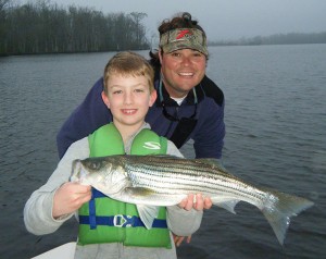 Capt. Richard Andrews helps Will Briley hoist a topwater striper from the Pamlico River.
