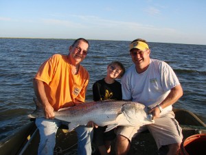 Men sit on a boat with a caught red drum.