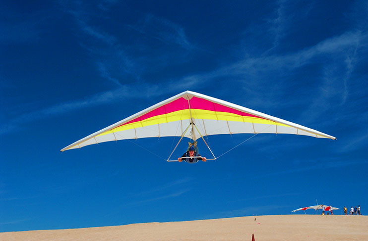 A hang glider flies above the sand.