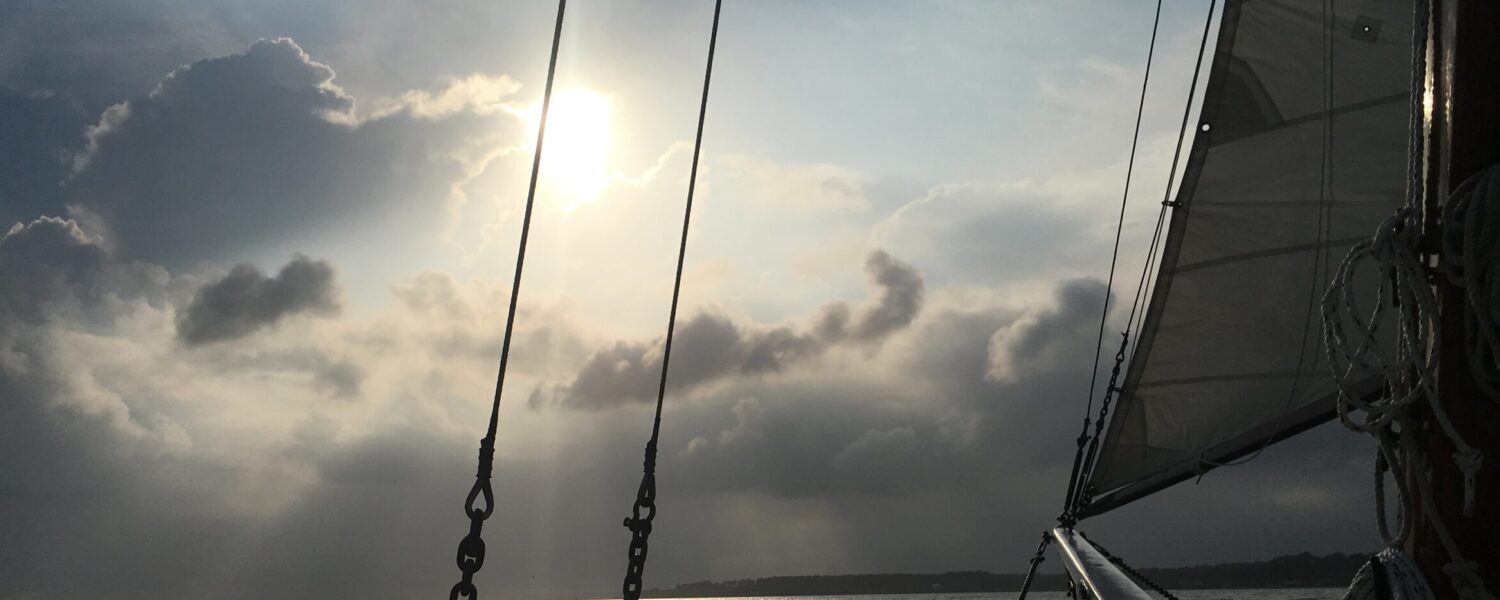 image: bow of a sailboat heads towards a cloudy horizon.