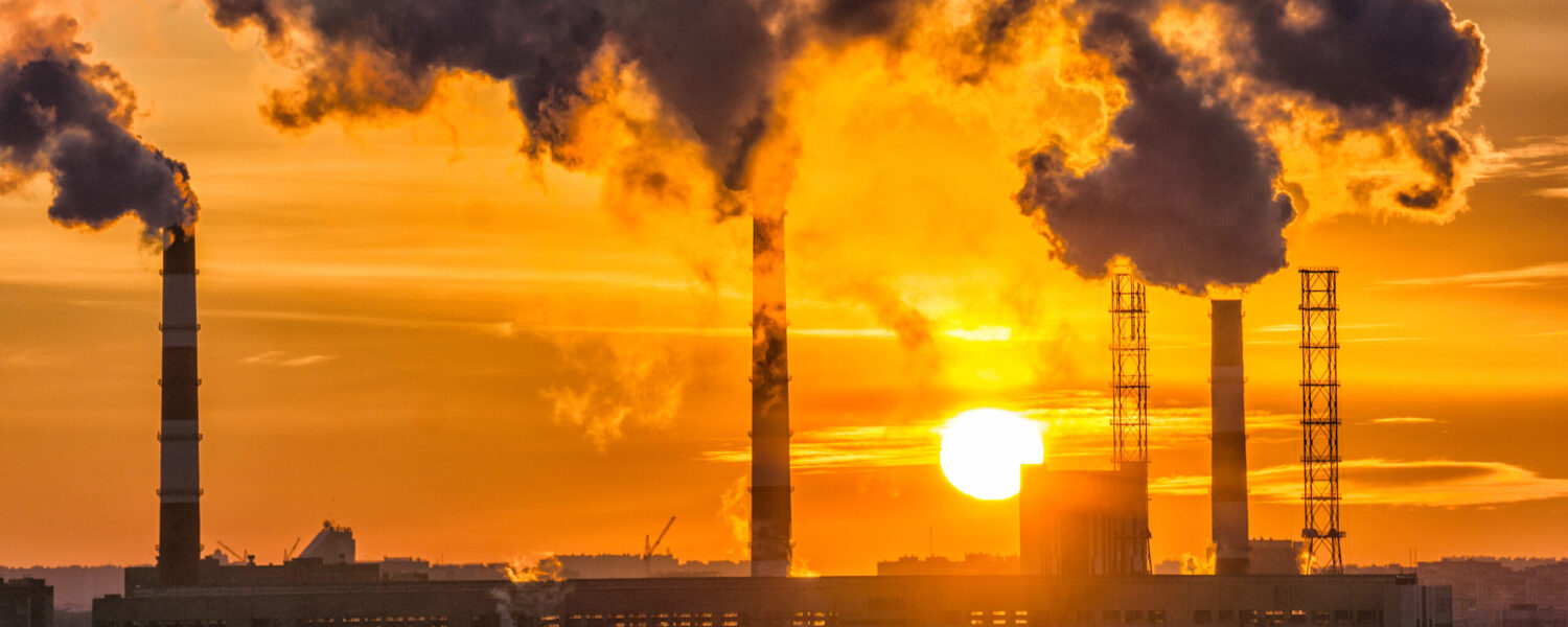 image: factory smokestacks release smoke into the air during sunset.