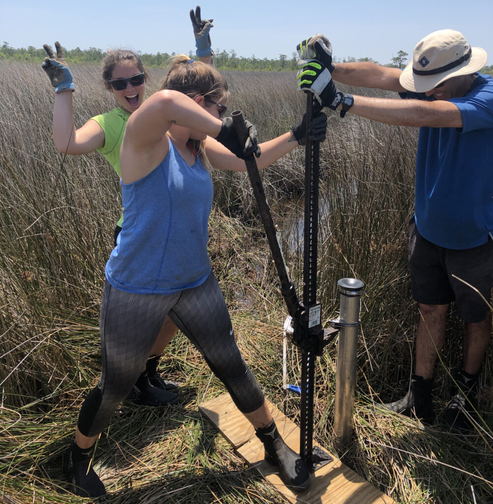 Carson Miller and Antonio Rodriguez pull a core out of the salt marsh with a ratchet jack. In the background, Molly Bost offers encouragement. Photo: Emily Eidam