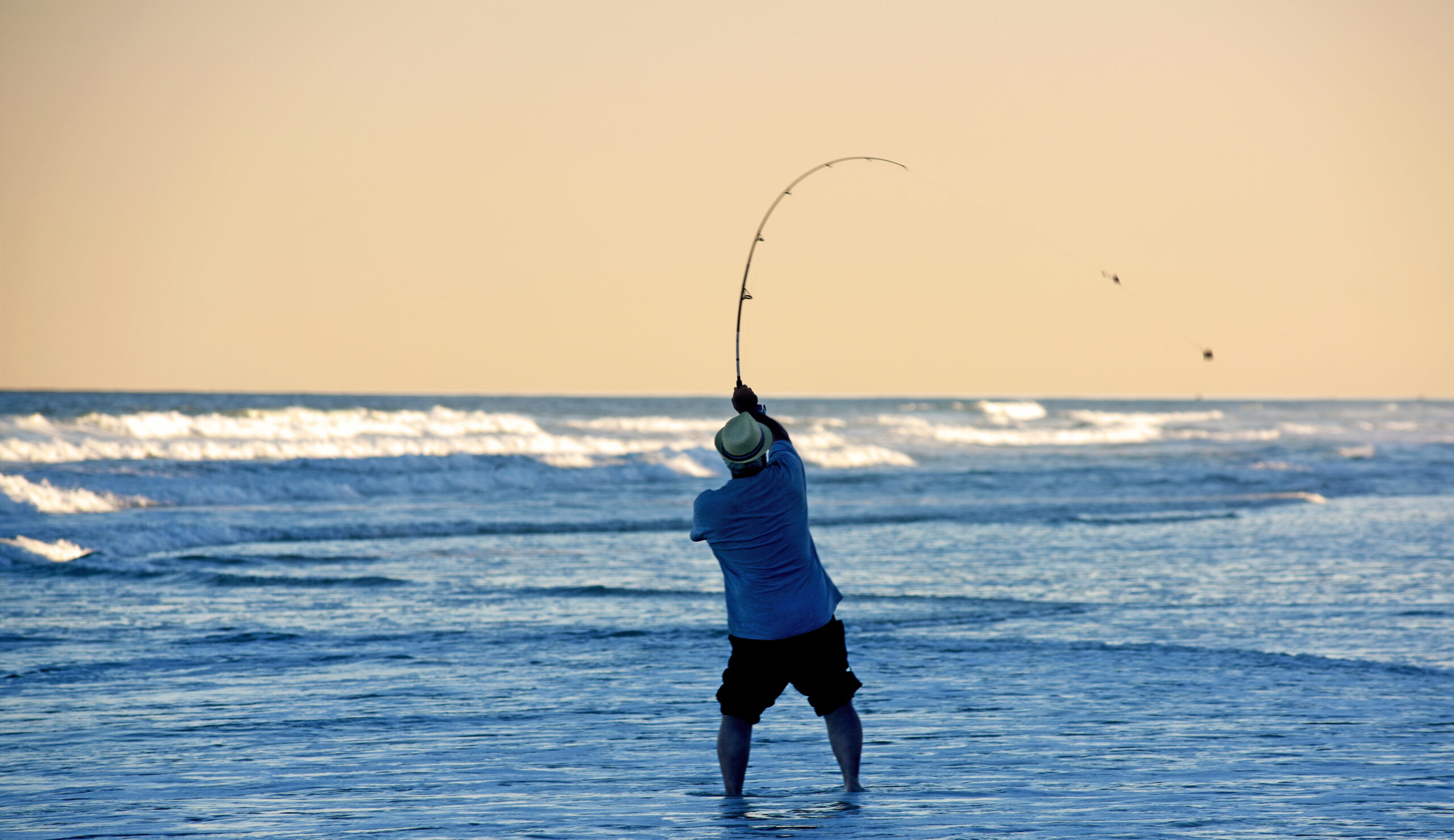 A fisherman casts into the surf as the sun sets along Carolina Beach.