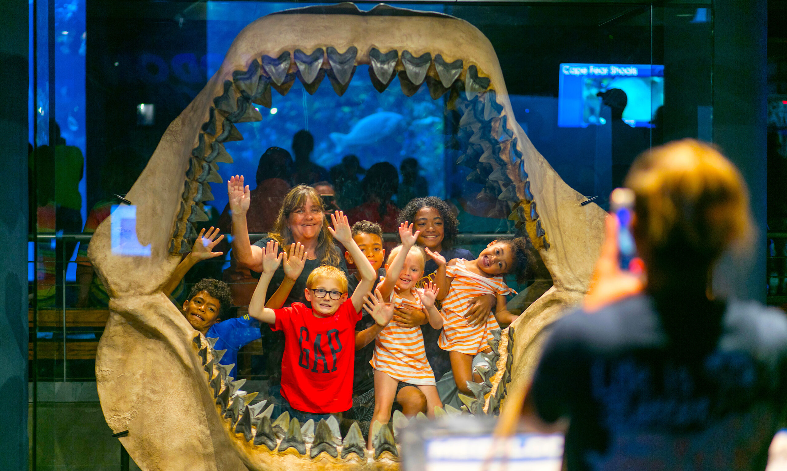 kids and teacher peer through the jaws of a megalodon shark
