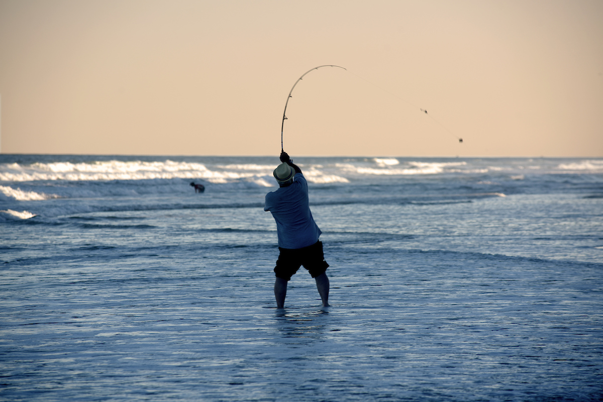 image: A fisher casts into the surf as the sun sets along Carolina Beach.