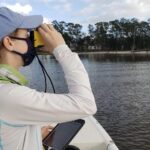 A girl in a blue hat and white shirt looks through binoculars while aboard a small boat