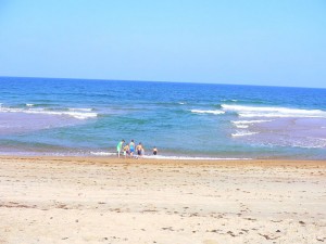 Adults and children standing on beach in front of rip current.