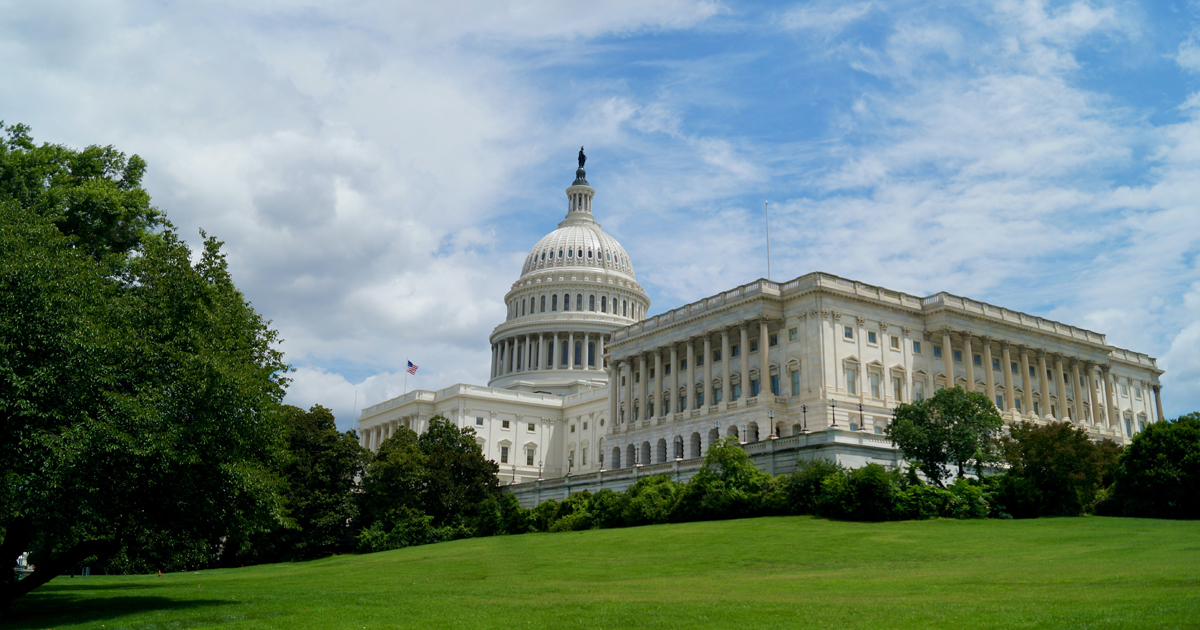 An image of the U.S. Capitol building, taken from the side, with trees in front and cloudy, blue skies above.