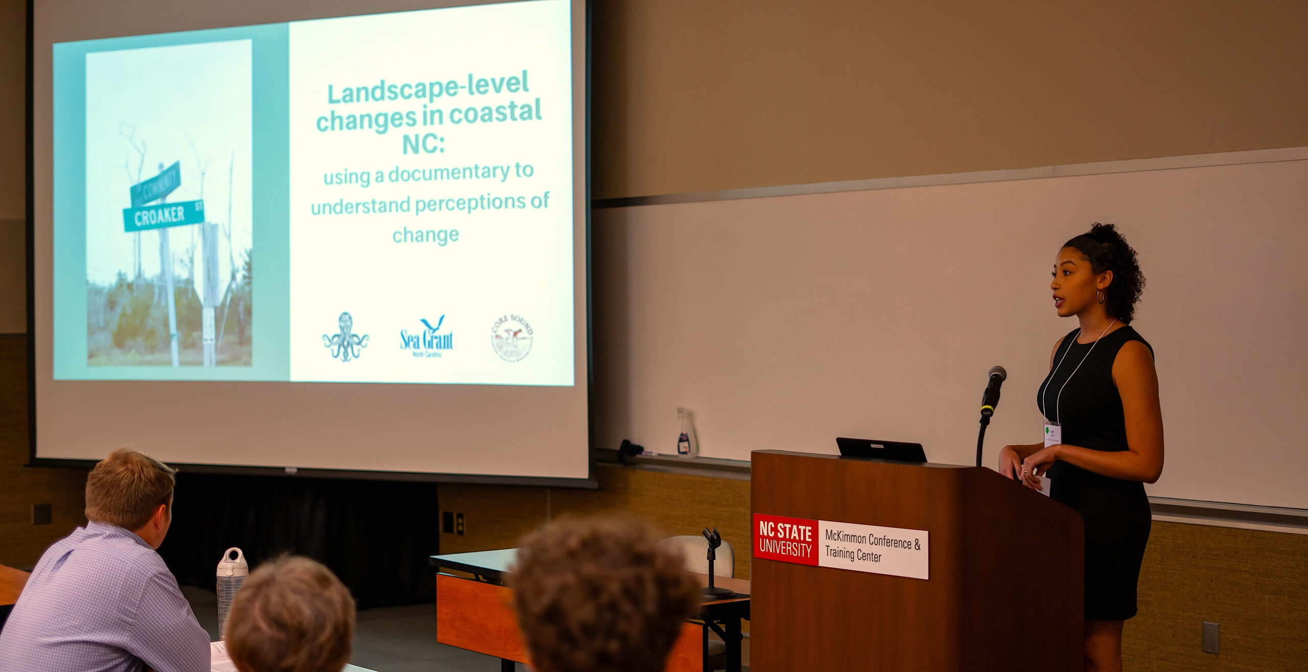 A woman standing at a podium giving a presentation in front of a screen