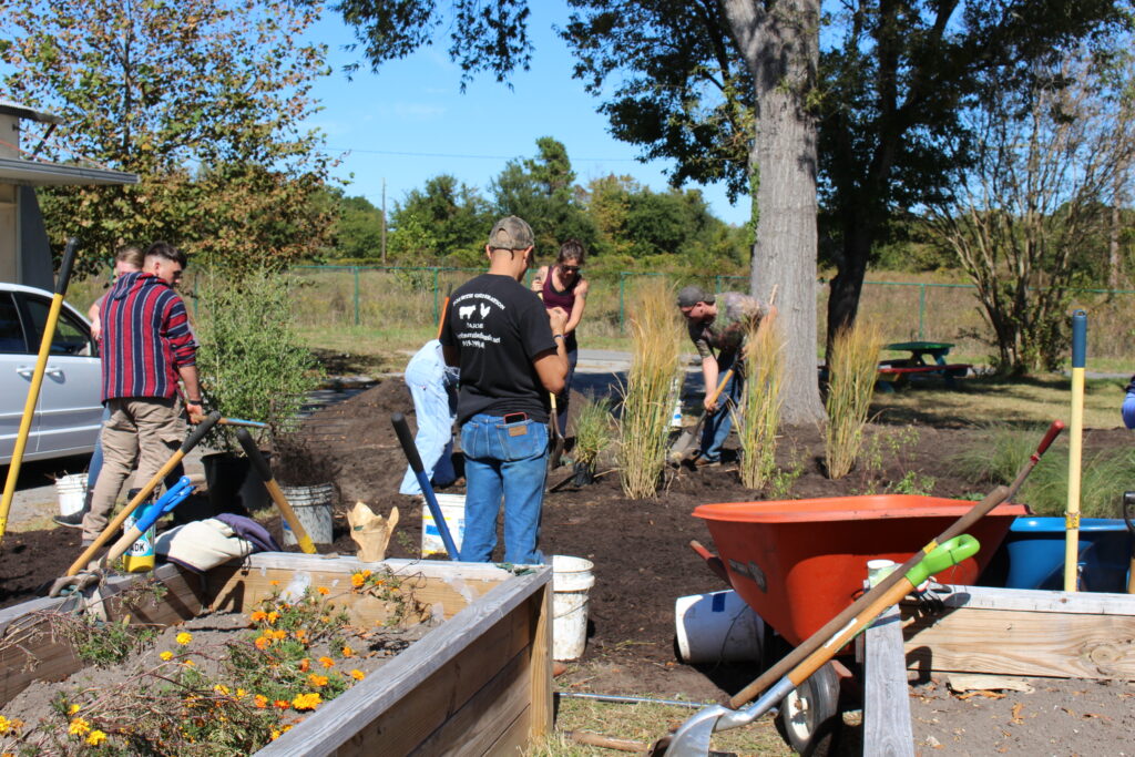 Volunteers plantng native plants surrounded by gardens and equipment