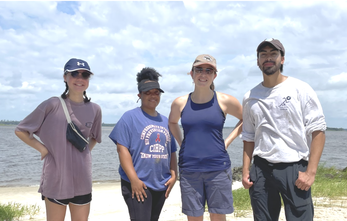 Photo of three of the four CEI interns from 2022 plus Jane Harrison, all standing in front of a coastline