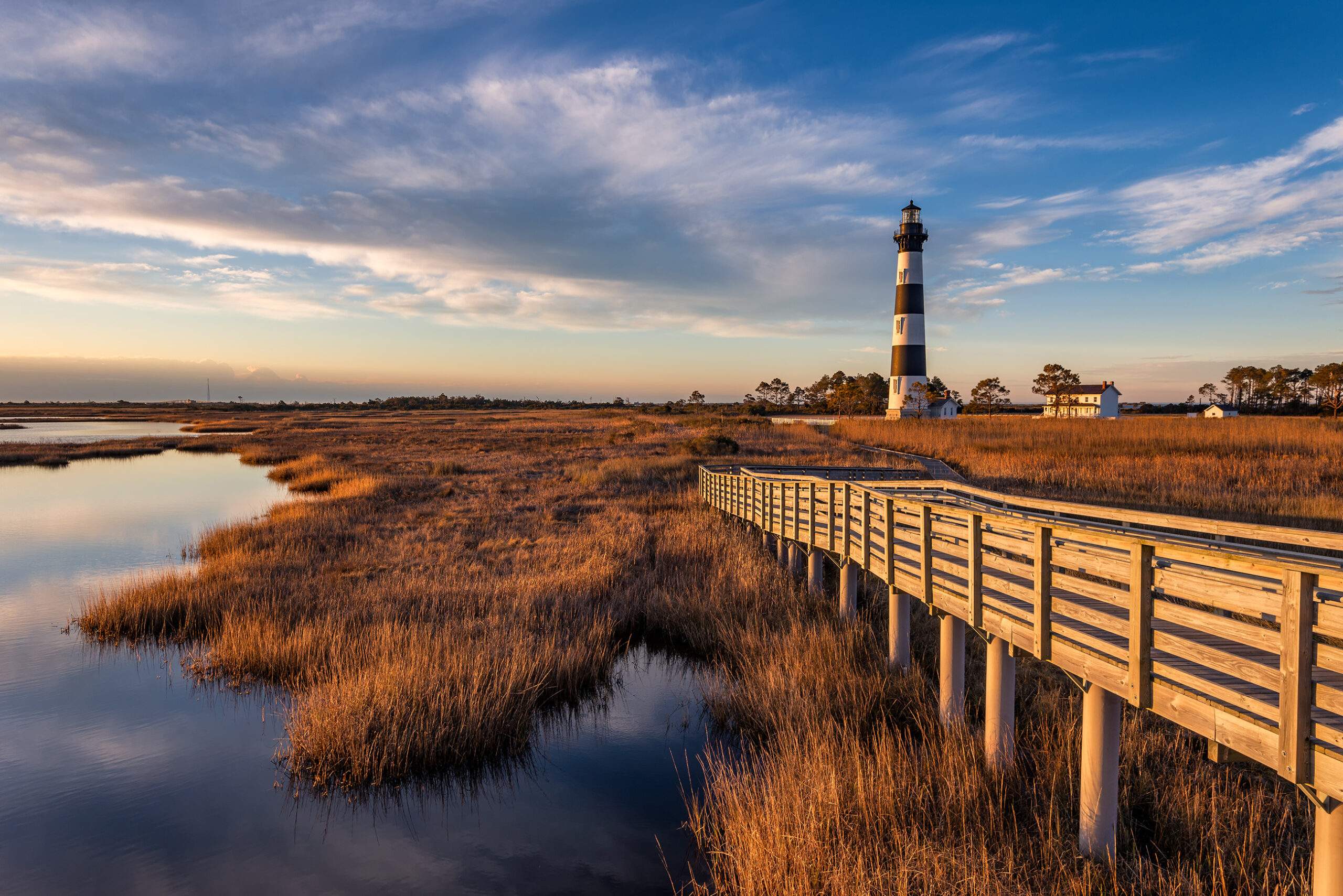 A wooden walkway leading to a lighthouse at sunset