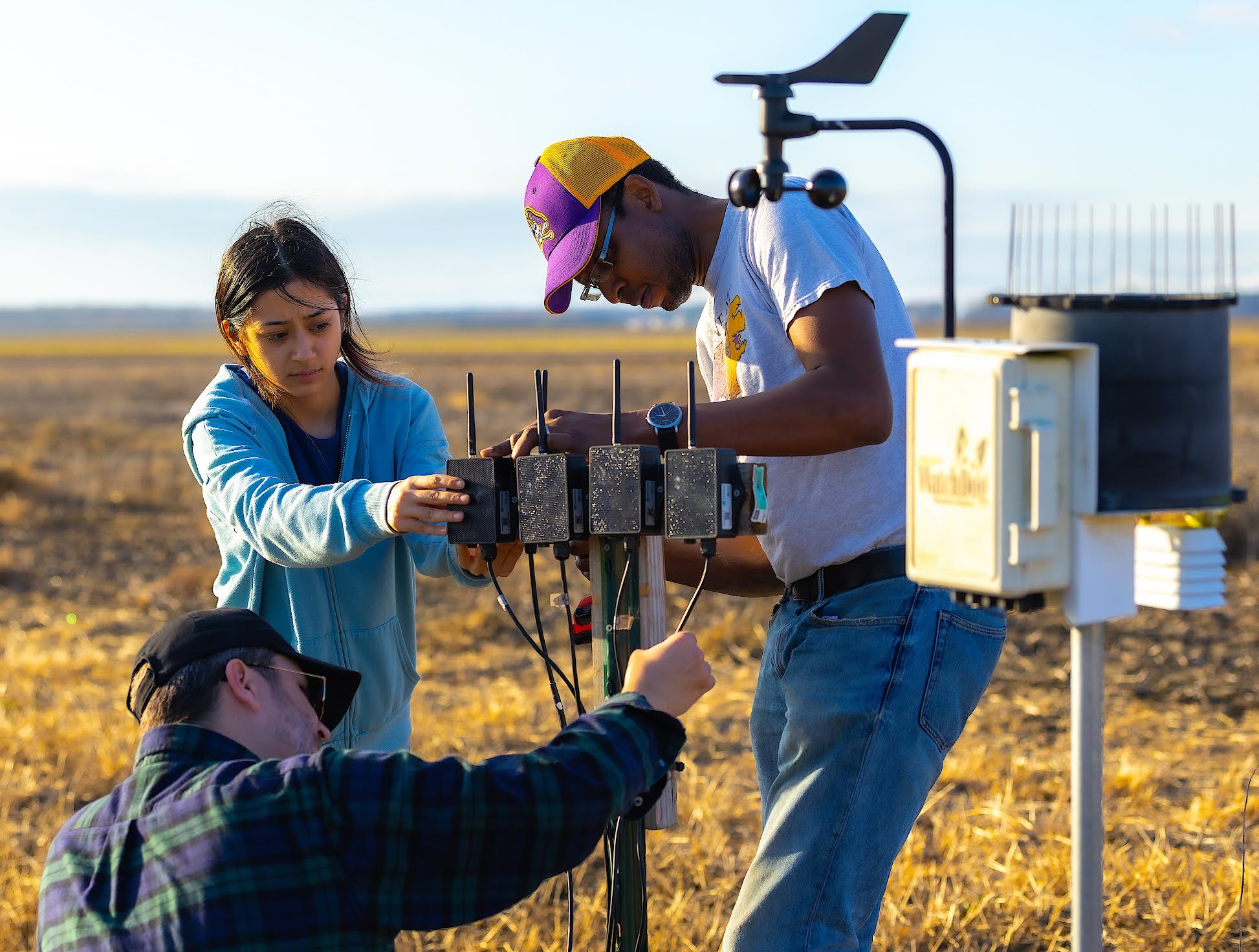 Three people working on getting a machine together out in a field to complete field work