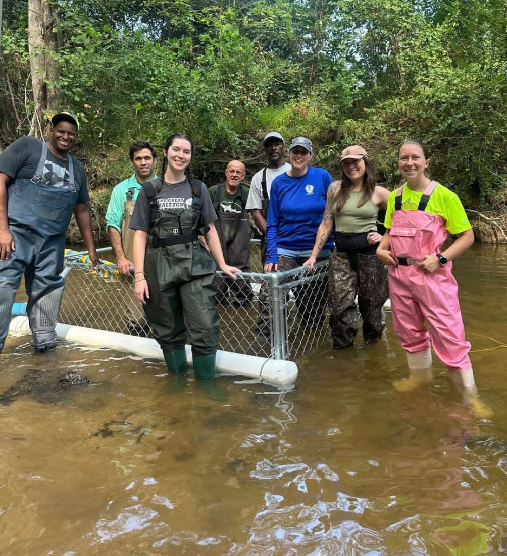 Volunteers from Great Raleigh Cleanup standing in front of a trash trap in a creek