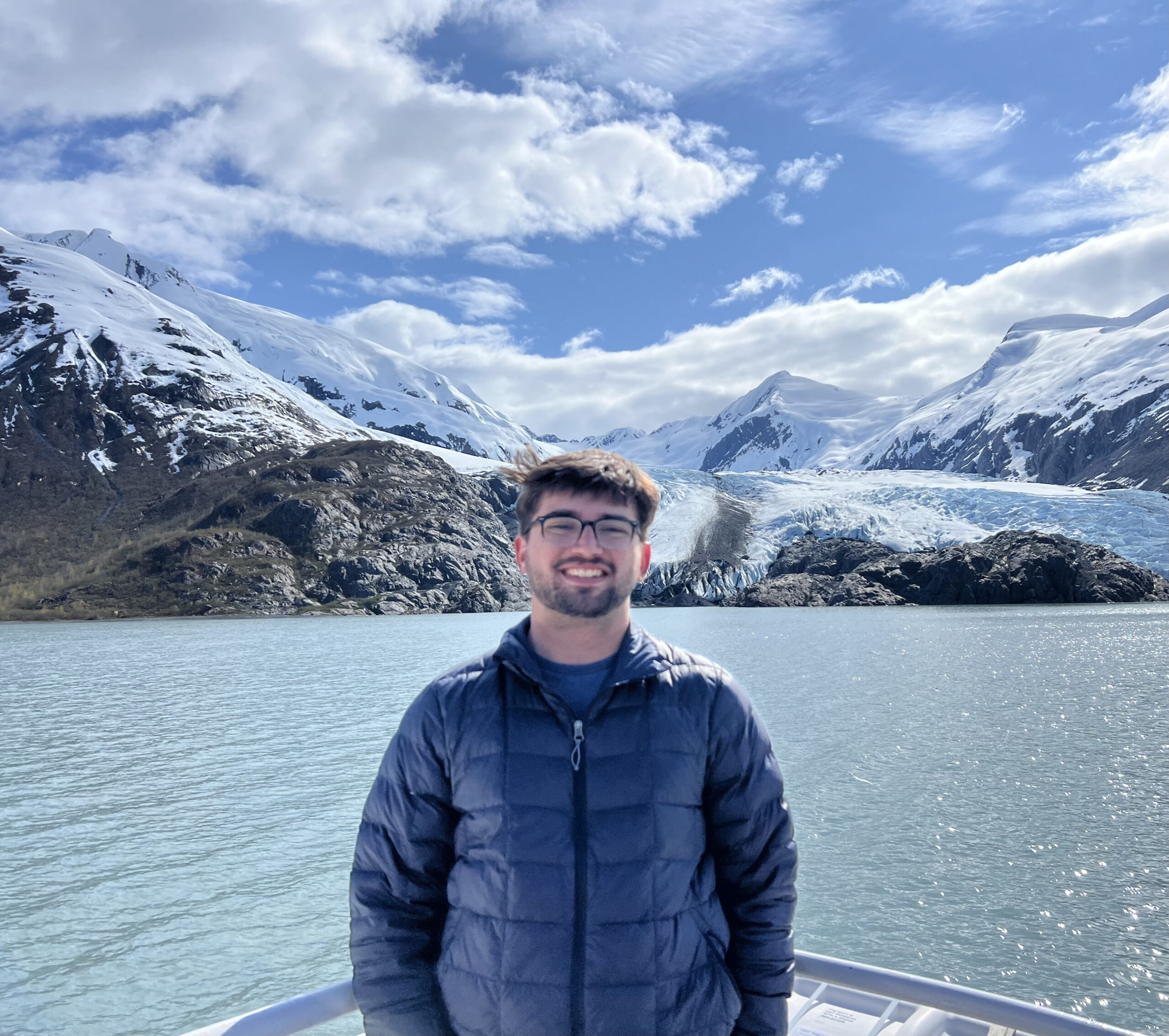 A man standing on a boat in the water in front of an icy glacier