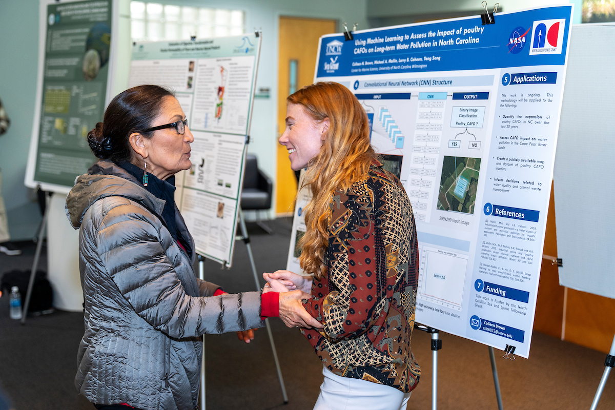 Two women talking in front of a science poster.