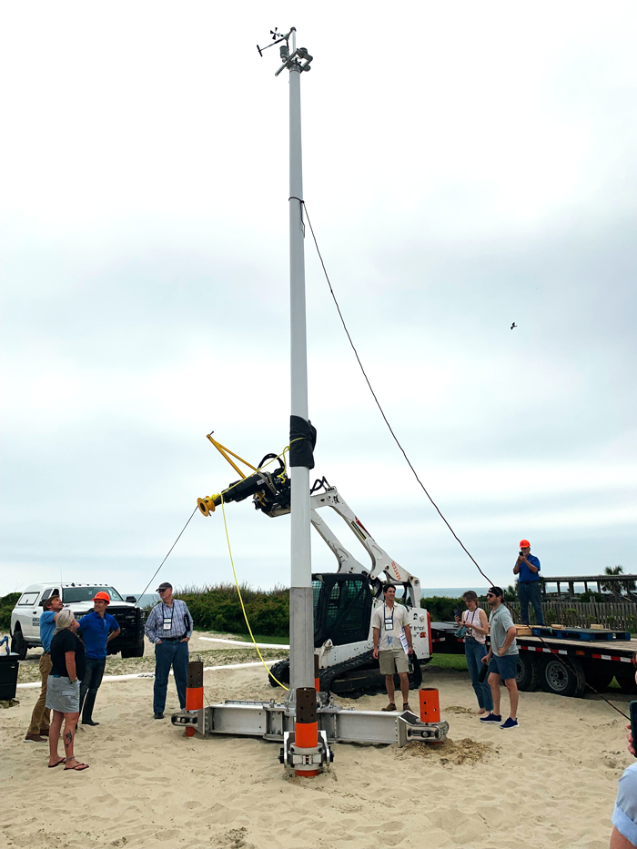 A sentinel tower on a beach with researchers and a construction vehicle nearby.