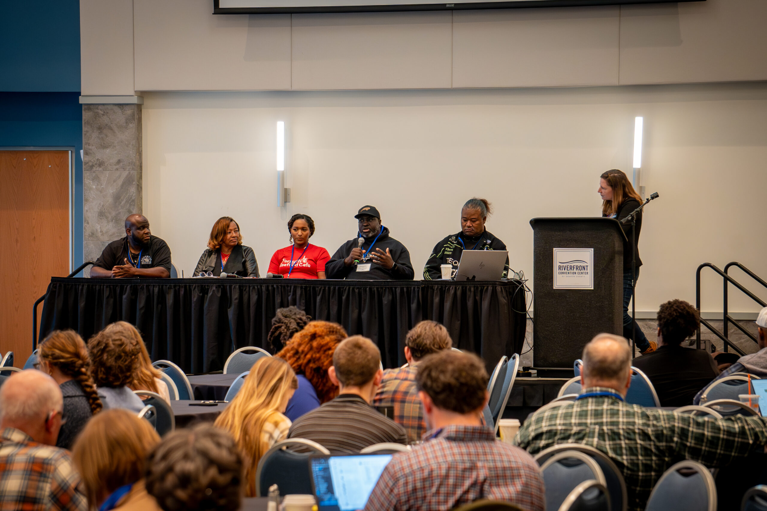 A panel discussion at a conference with five panelists and an audience.